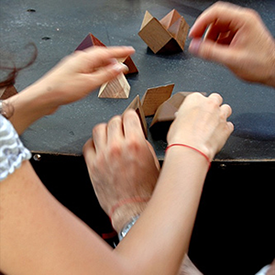 Photograph of 2 pairs of hands collaborating by assembling different shaped blocks.