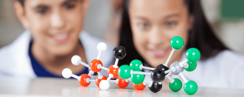 molecule model with a boy and a girl students wearing lab coats in the background