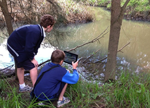 Photo of children using ipad to film or photograph a pond.