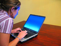 girl working at a laptop with fingers on the keypad and the blue light from the screen refelcting on her face