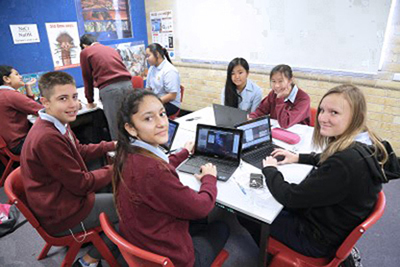 Decorative image of children in a classroom with laptops and text books.