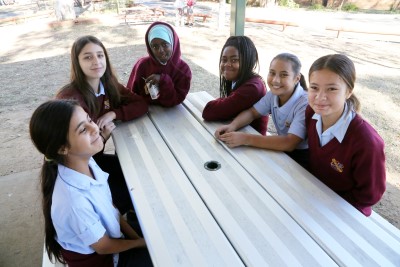 Decorative image of a group of children sitting at a table in a school playground.