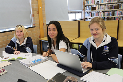 Decorative image of 3 children in a classroom with a laptop and books.