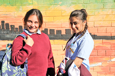 Decorative image of 2 children standing in front of a mural on a school building.