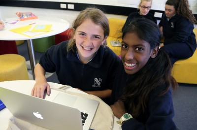 Decorative image of 2 children in a classroom working with a laptop computer.