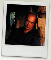 Photograph of William Dalrymple. He is wearing a black shirt and leaning against a brick wall.