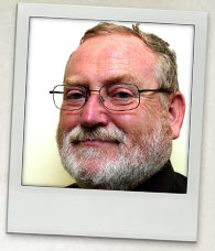 Photograph of Ross Gittins. He has grey hair, a beard and wears glasses.