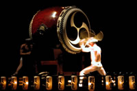 Taiko thumbnail: two men beat the skin of a very large drum with sticks.