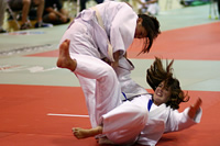 Judo thumbnail: Two girls white judo suits compete in a tournament; one has fallen on her back, legs, arms and hair flying