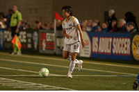Soccer thumbnail: a young woman in a sports uniform poised ready to kick a soccer ball as spectators watch on