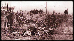 Soldiers in a field, one is lying on the ground next to a bicycle.
