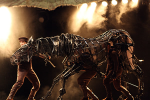 Two men support a life-size puppet horse and another holds its head.