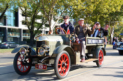 A vintage car with three old men, two are waving and one is wearing lots of medals.