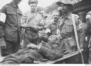 Man lying on a stretcher carried by a soldier with a red cross arm band.