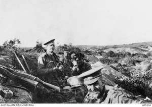 Soldiers in an open trench look at the camera. Rifles are resting on the bank.