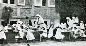 Adults attending to children seated at long rows of tables.