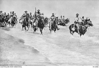 Men in uniform riding horses through shallow water