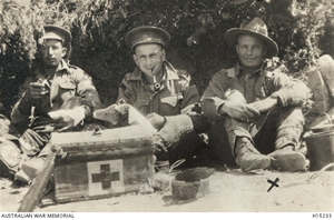 Soldiers sitting in the shade with a Red Cross box in front of them.