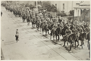 Row of men on horseback riding down a street