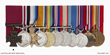 A row of medals mounted on ribbons; the first, a bronze cross on a crimson ribbon, is marked as the Victoria Cross