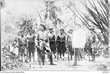 Three white men, two in uniform, standing in front of a group of PNG men carrying rifles and wearing military style caps and belts.