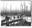 Five Australians walk along a wooden track over mud and water among gaunt bare tree trunks devastated by battle.