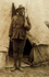 Photo of an Aboriginal man in front of a tent holding a rifle