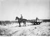 A soldier on a horse pulling a cart with another man sitting inside. The ground around are flat and possibly covered in snow.