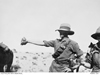 A soldier wearing a large hat holds a pigeon in his outstretched hand.