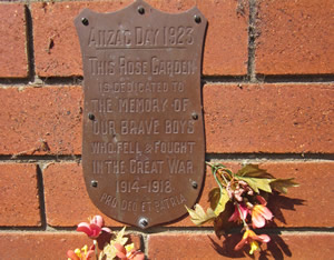 Plaque on a brick wall with some flowers. The plaque reads: 'Anzac Day 1923—This rose garden is dedicated to the memory of our brave boys who feel and fought in The Great War 1914-1915 – Pro deo et patria'