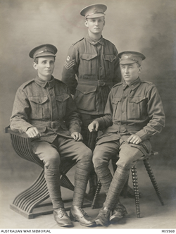 Three young men in uniform, two seated, pose for photographic portrait